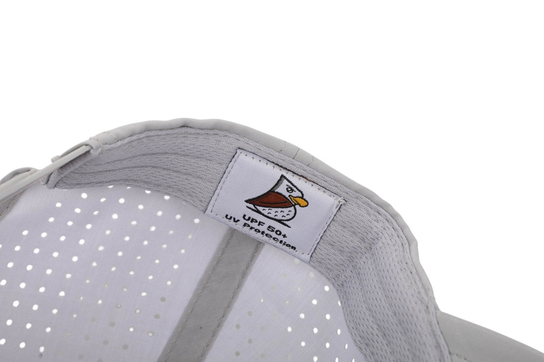 Close-up of the Gray Eagle | Golf Hat interior, displaying a label with an illustrated bird and UPF 50+ UV Protection. The light gray cap features small ventilation holes and moisture-wicking fabric for comfort.