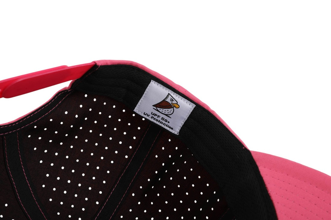 Close-up of the Reverse Baja | Golf Hat in pink, showing a bird logo label with UPF50+ sun protection. Features a black and white dotted inner lining and offers moisture-wicking comfort for sunny days.