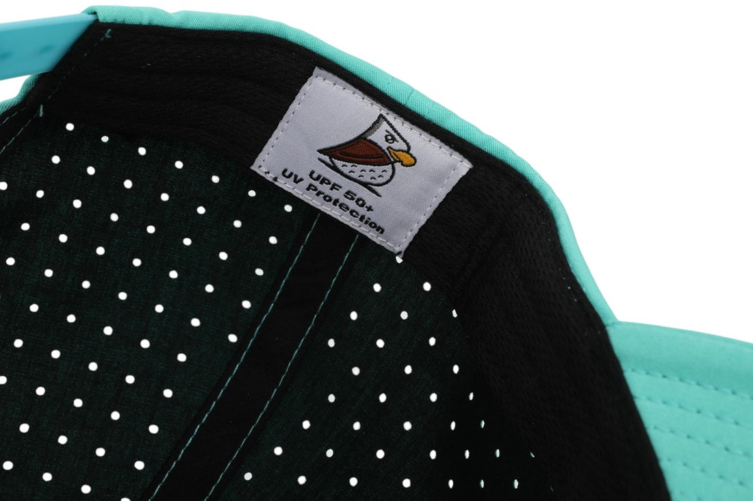 Close-up of the Baja | Golf Hat in turquoise, showing a black moisture-wicking inner lining with white polka dots, plus a label with a bird logo and UPF50+ UV protection.