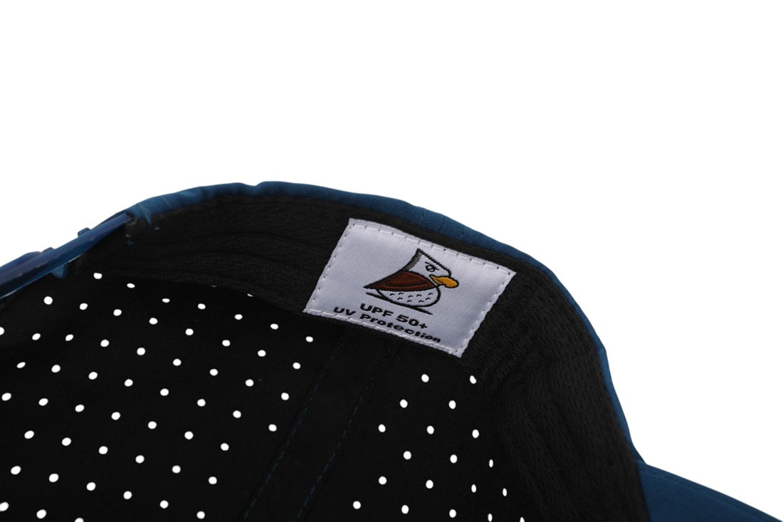 Close-up of the Eagle PS | Rope Golf Hat (Demo Listing) in blue, featuring a white label with a bird logo and “UPF 50+ UV Protection.” The black inner lining with white polka dots offers stylish sun protection.