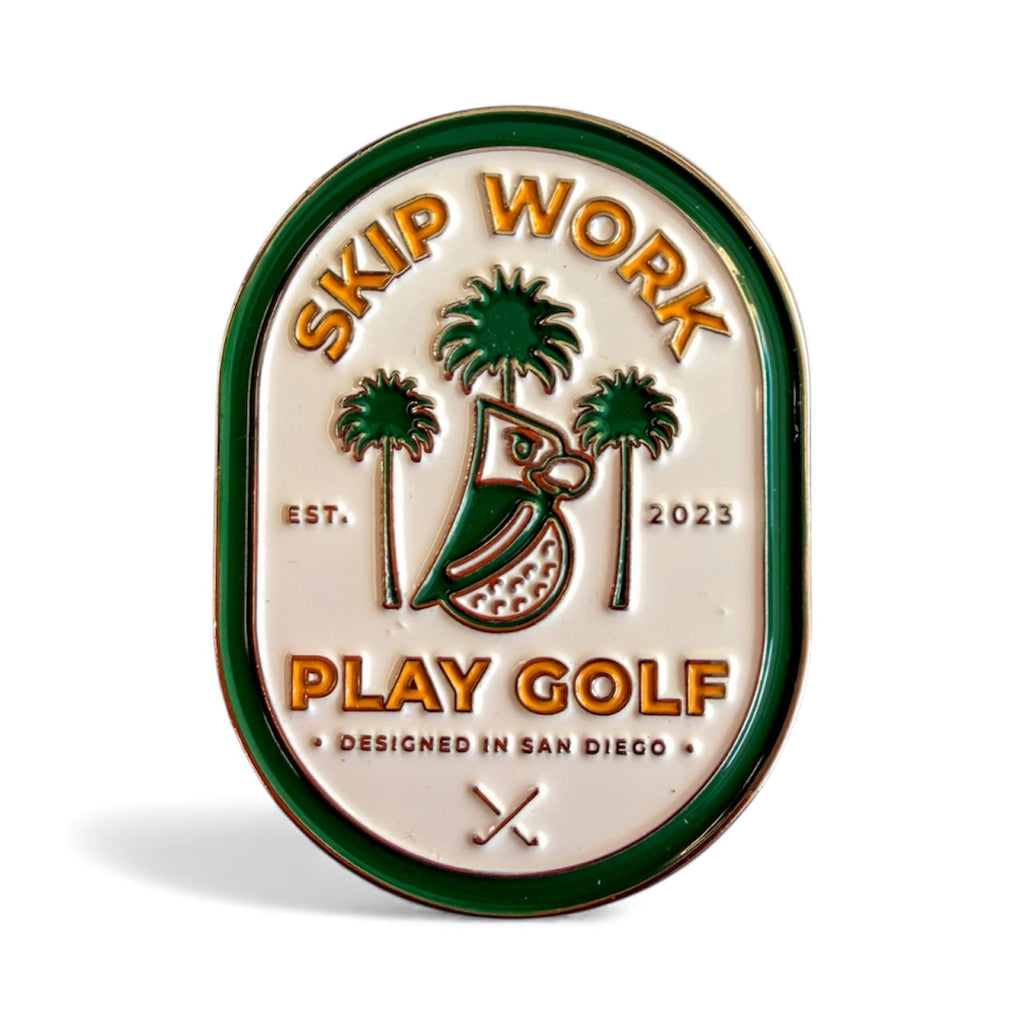 The Skip Work Ball Marker is an oval premium metal marker with green and gold trim, a stylized bird, palm trees, golf clubs, and text: “Skip Work Play Golf,” “EST. 2023,” and “DESIGNED IN SAN DIEGO.” Perfect for golfers!.