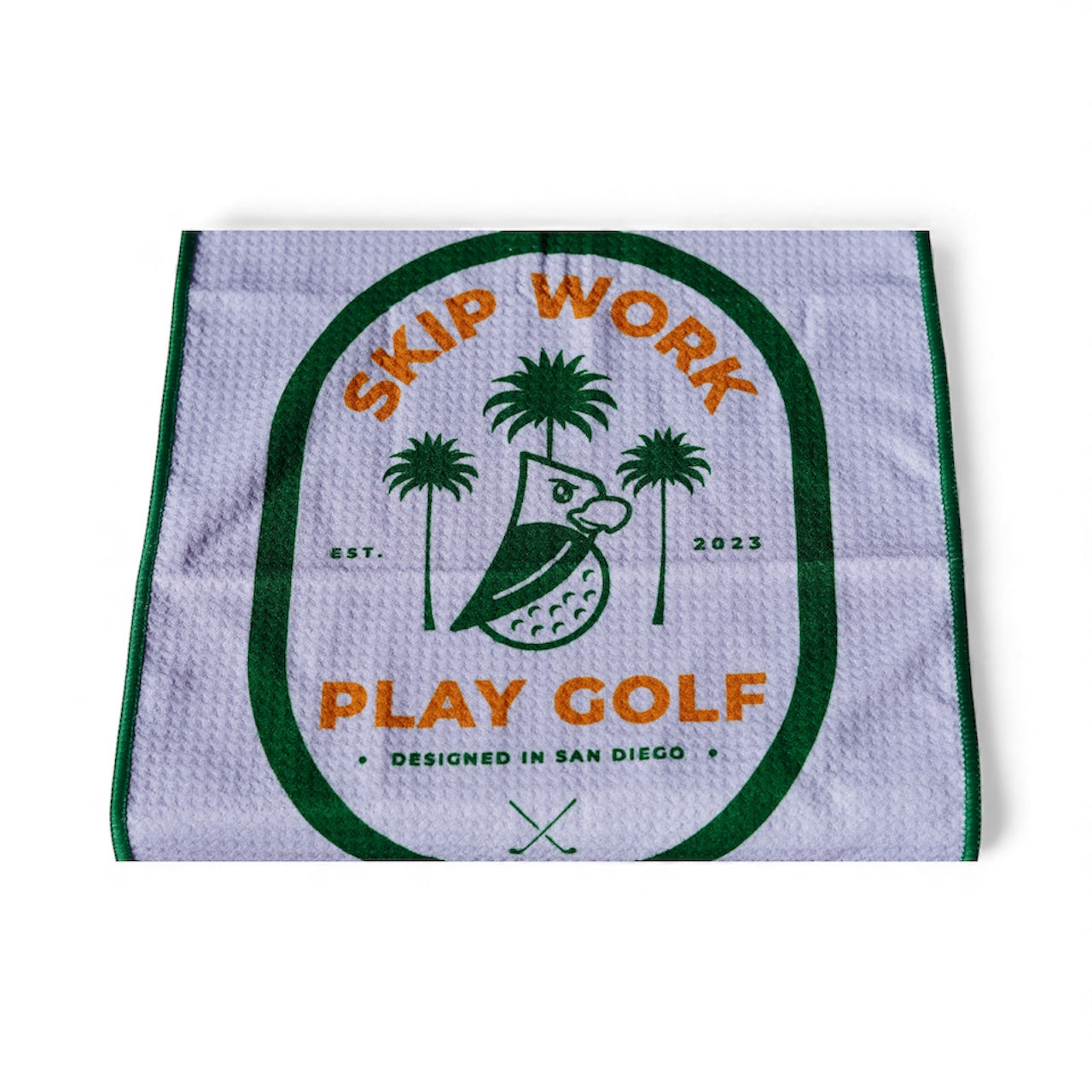 The Skip Work Bundle includes a white waffle golf towel with green and orange trim featuring an owl, palm trees, “SKIP WORK PLAY GOLF,” two crossed clubs, “EST. 2023,” and “DESIGNED IN SAN DIEGO.”.