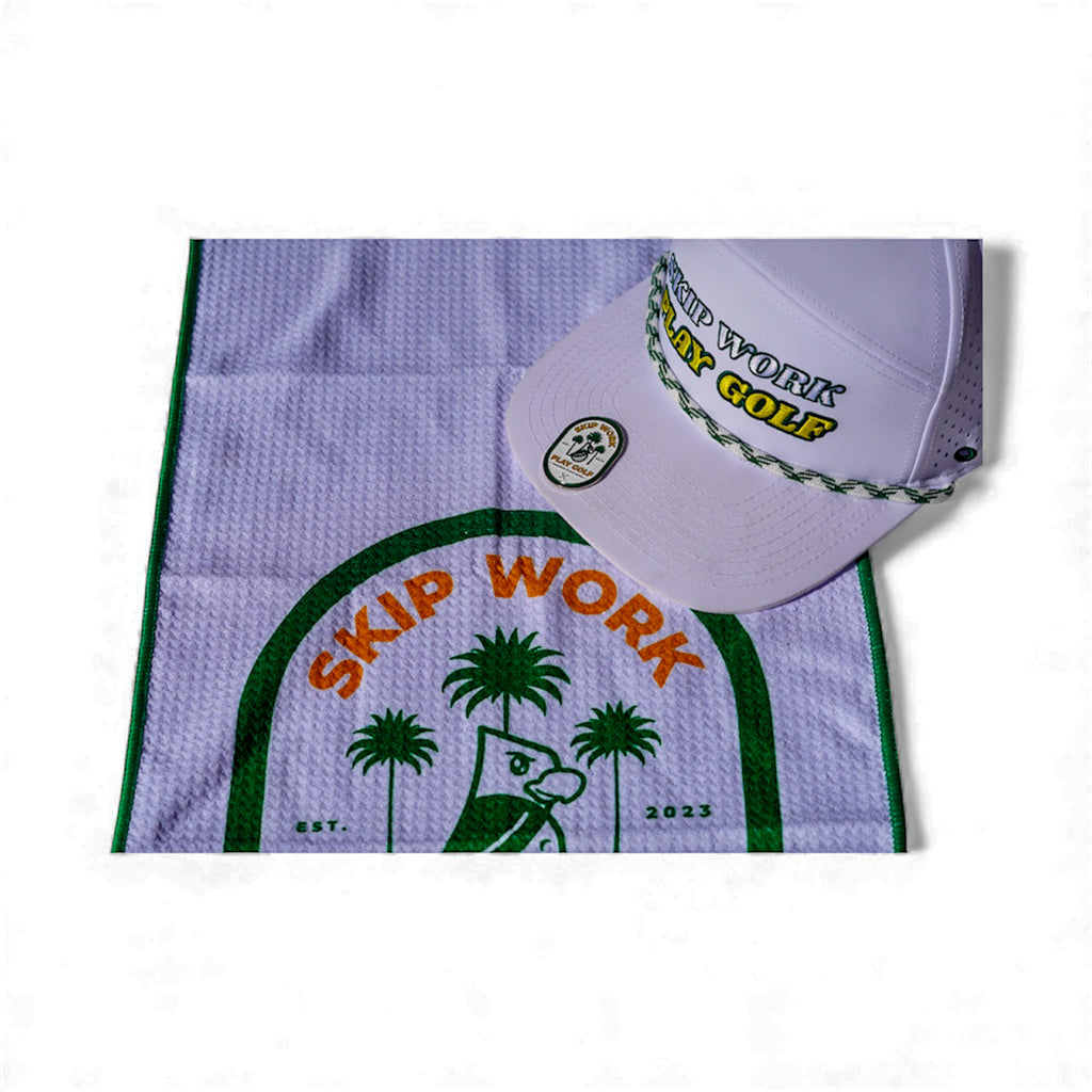 The Skip Work Bundle includes a lavender waffle golf towel with green border featuring a cartoon duck, palm trees, and "SKIP WORK," plus a white golf hat with "SKIP WORK PLAY GOLF" embroidered and a green braided rope above the brim.