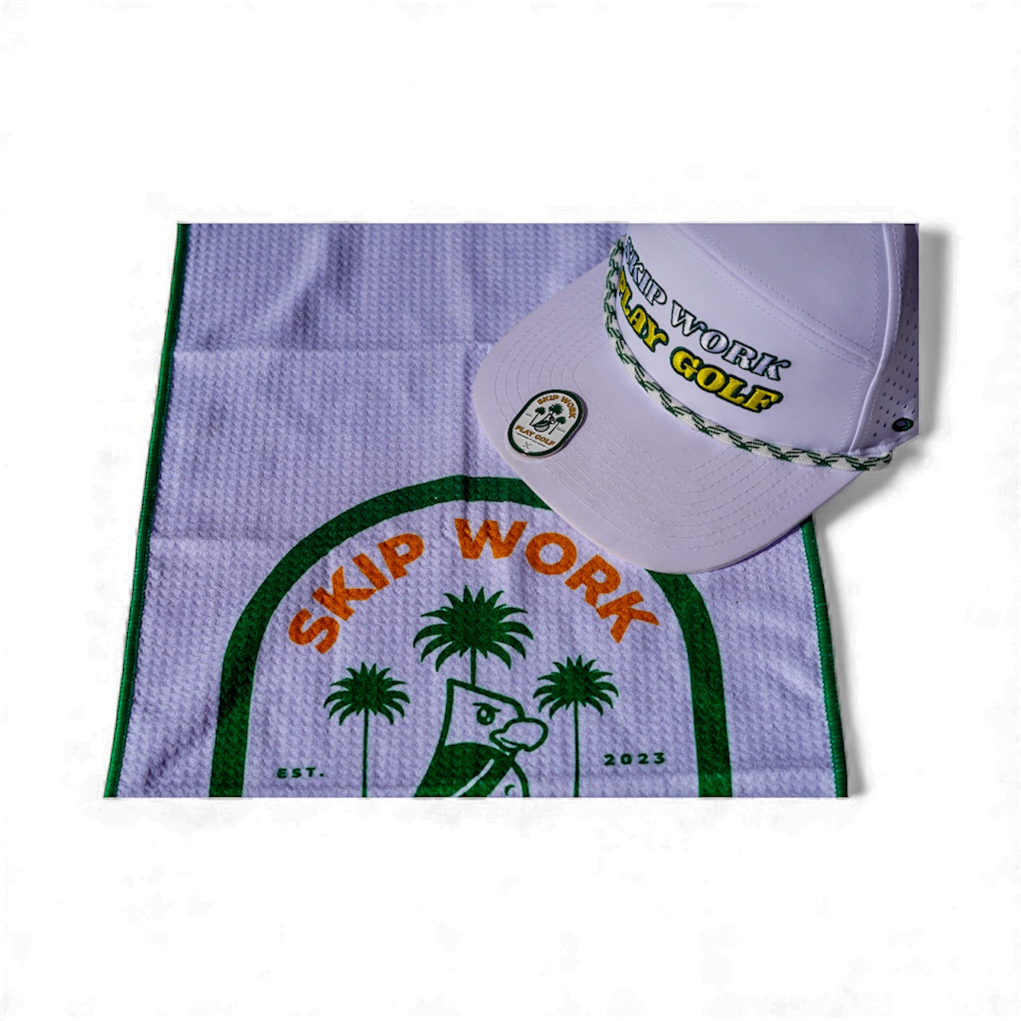 The Skip Work Bundle includes a lavender waffle golf towel with green border featuring a cartoon duck, palm trees, and "SKIP WORK," plus a white golf hat with "SKIP WORK PLAY GOLF" embroidered and a green braided rope above the brim.